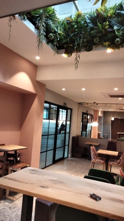 Restaurant dining area in dusty pink under a planted skylight